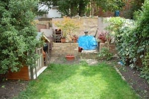 A backyard garden sketch featuring green grass, potted plants, a small shed, and a stone patio area partially covered by a blue tarp.