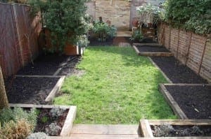A sketch of a rectangular backyard garden features a central grass lawn, surrounded by wooden raised beds filled with soil and bordered by wooden fences.