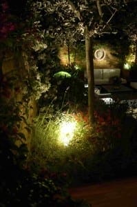 A Night Garden scene features illuminated plants, shrubs, and a tree with accent lighting, set against a brick wall with patio seating in the background.