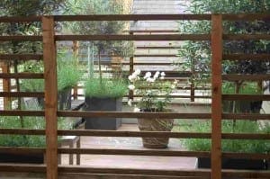 A wooden slat fence partially obscures a small Mondrian Garden patio with potted plants and white flowers in an urban setting.