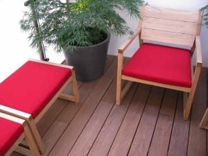 Wooden chair and footstool with red cushions on a wooden deck, beside a potted green plant and vibrant Acers.