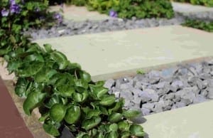 Green leafy plants border light stone slabs and gray gravel, highlighting the garden pathway's natural stone textures.