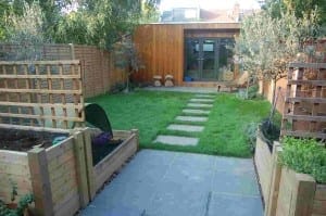 A modern backyard garden designed with outdoor rooms, featuring a wooden shed, raised beds, a patio, stepping stones across a lawn, and wooden fencing.