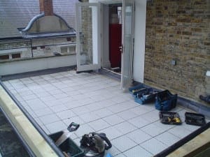 A rooftop terrace under construction with tools and equipment on a tiled floor, next to an open door leading inside a brick building—soon to become a Mondrian Garden-inspired retreat.