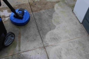 A patio is being cleaned with a blue surface cleaner, showing a clear difference between the cleaned and dirty paving slabs—perfect for those who enjoy outdoor activities like composting in a tidy garden space.