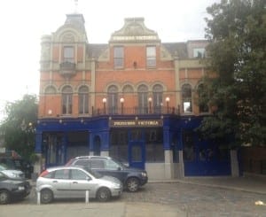 A three-story brick building in Shepherd’s Bush with “Princess Victoria” signage, a blue ground floor facade, arched windows, and several parked cars in front.