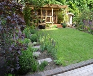 A well-maintained garden with a green lawn, flower beds, shrubs, stepping stones, and a stunning wooden pergola gracing the background.