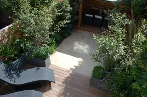 A modern garden patio with wooden decking, black lounge chairs, potted plants, and a shaded seating area—perfect for small spaces thanks to smart designs that maximize comfort and style.