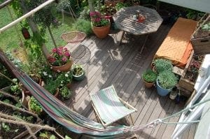 A wooden deck with potted plants, a striped hammock, a striped lounge chair, an octagonal table, and a bench with an orange cover—featuring smart designs perfect for small spaces among garden items.