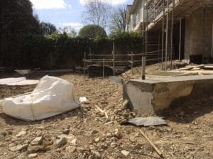 A construction site with exposed soil, scattered debris, builders’ materials, and scaffolding adjacent to a partially built structure where the front garden is yet to take shape.